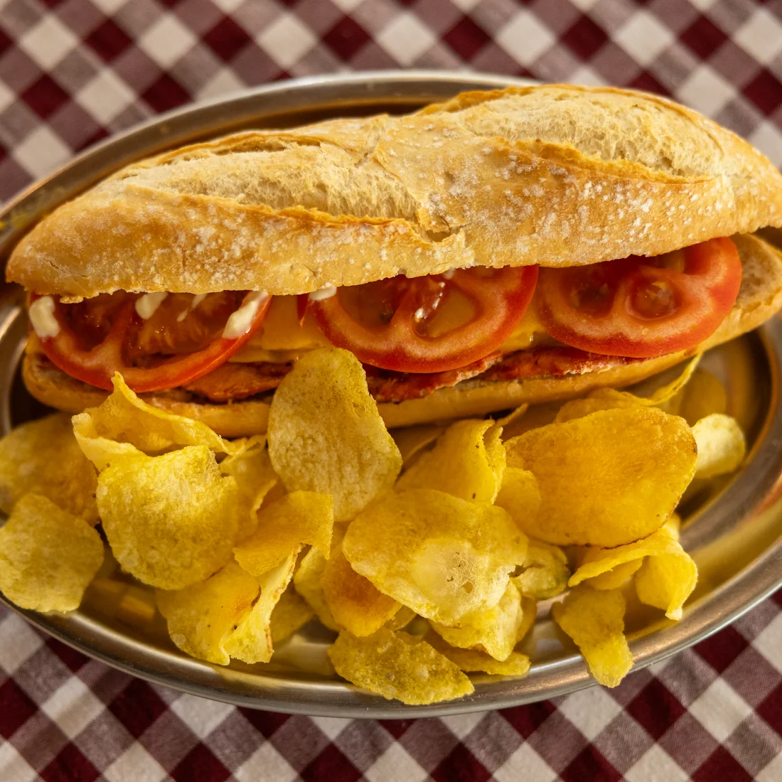 Pepito de ternera con queso y tomate sobre bandeja con patatas